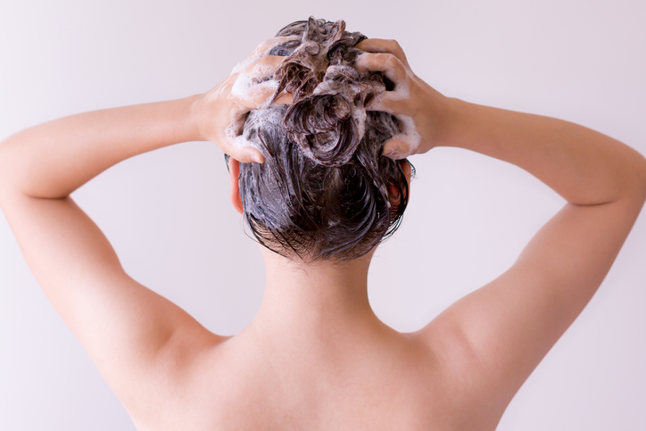 Young woman. Back shot. Hands on back of head. Hair has many suds from shampoo